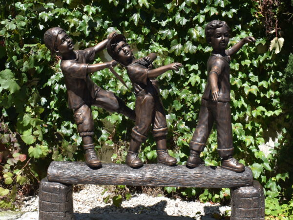 A lovely bronze statue of three children walking on a log