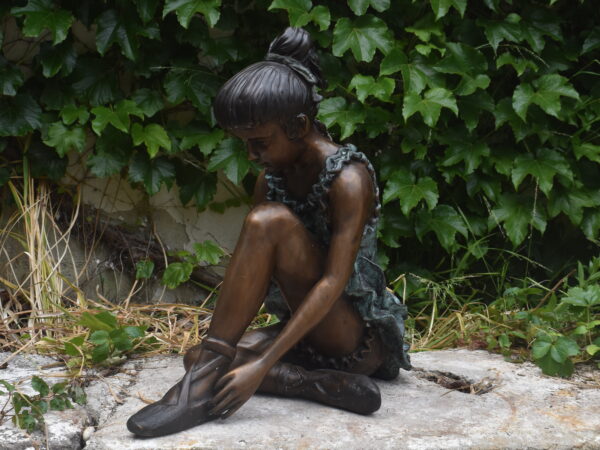 a bronze sculpture of a girl tying her shoe. 