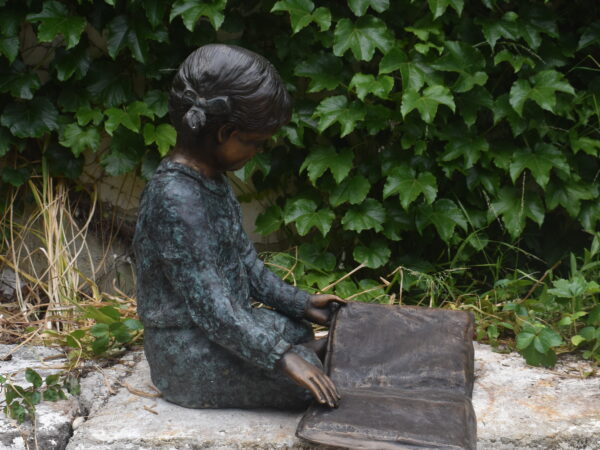 a bronze sculpture of a girl reading a book