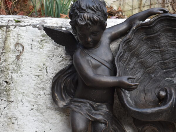 A classic bronze fountain with cherubs holding a shell, water pours from each side of the shell.