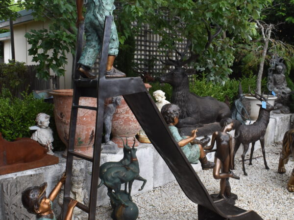 A large bronze sculpture of 3 children playing on a slide
